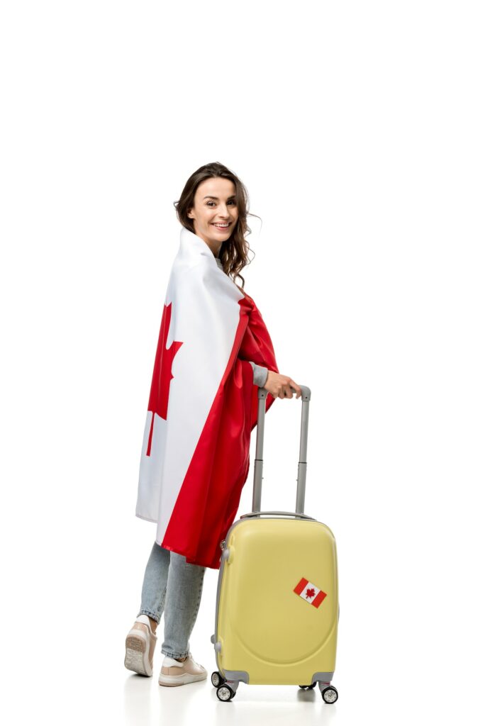 smiling woman covered in canadian flag with suitcase isolated on white, travel concept
